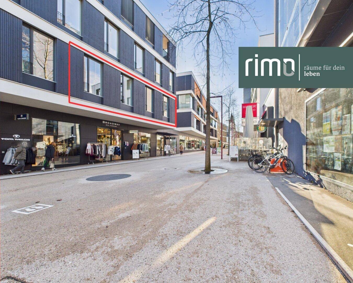 Ansicht eines modernen Gebäudekomplexes mit großen Fenstern und Geschäften im Erdgeschoss.