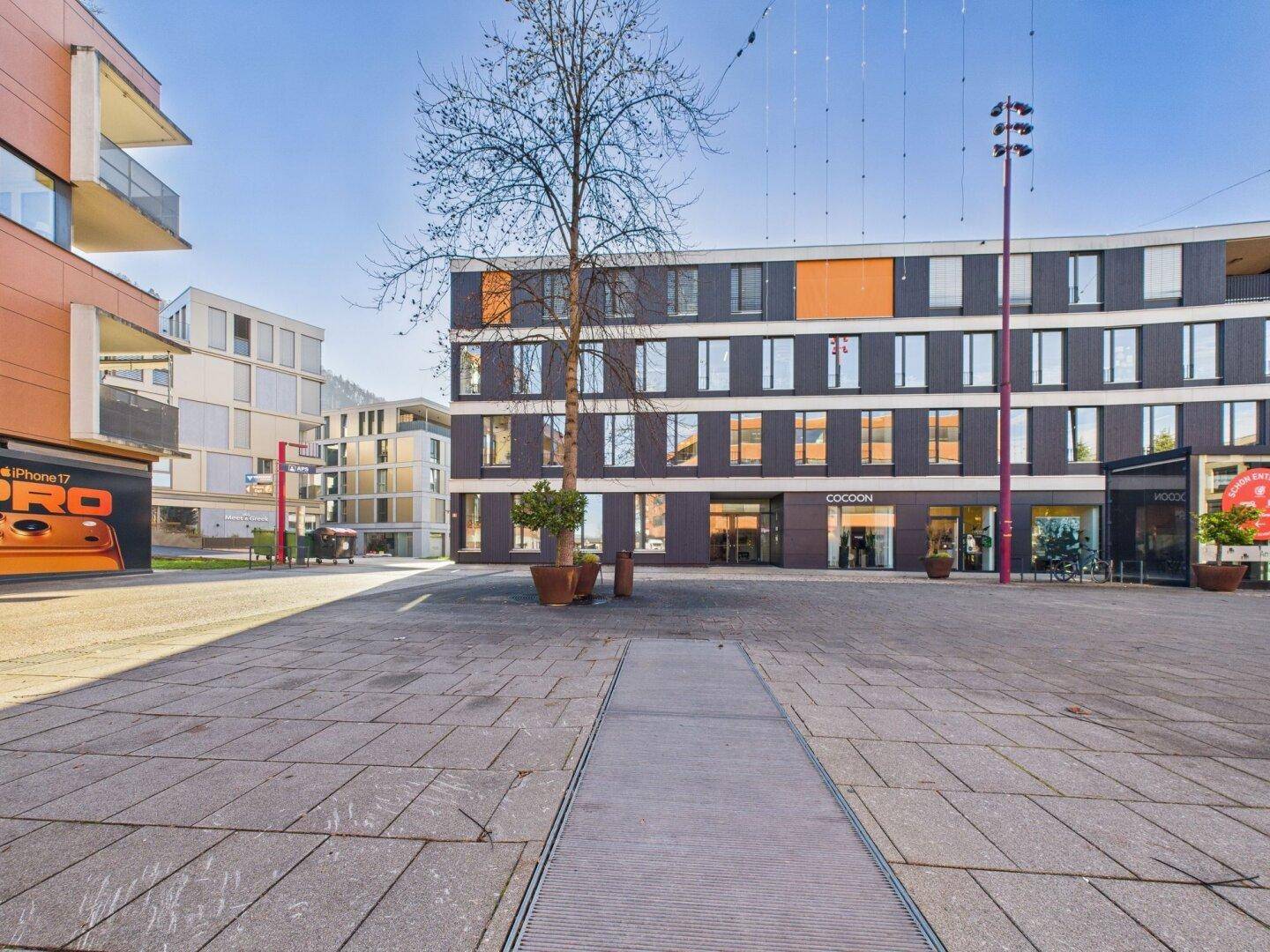 Moderner Gebäudekomplex um einen gepflasterten Platz mit Geschäften und Wohnungen.