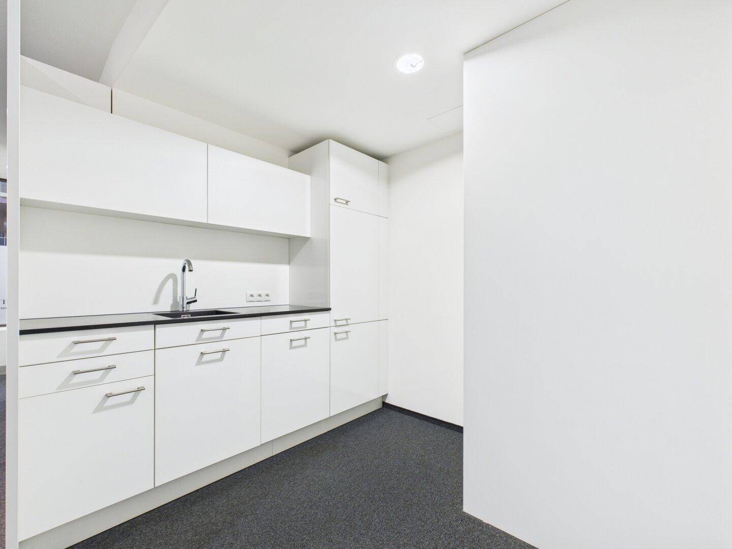 Funktionale, moderne Teeküche mit weißen Schränken, schwarzer Arbeitsplatte und Spülbecken.