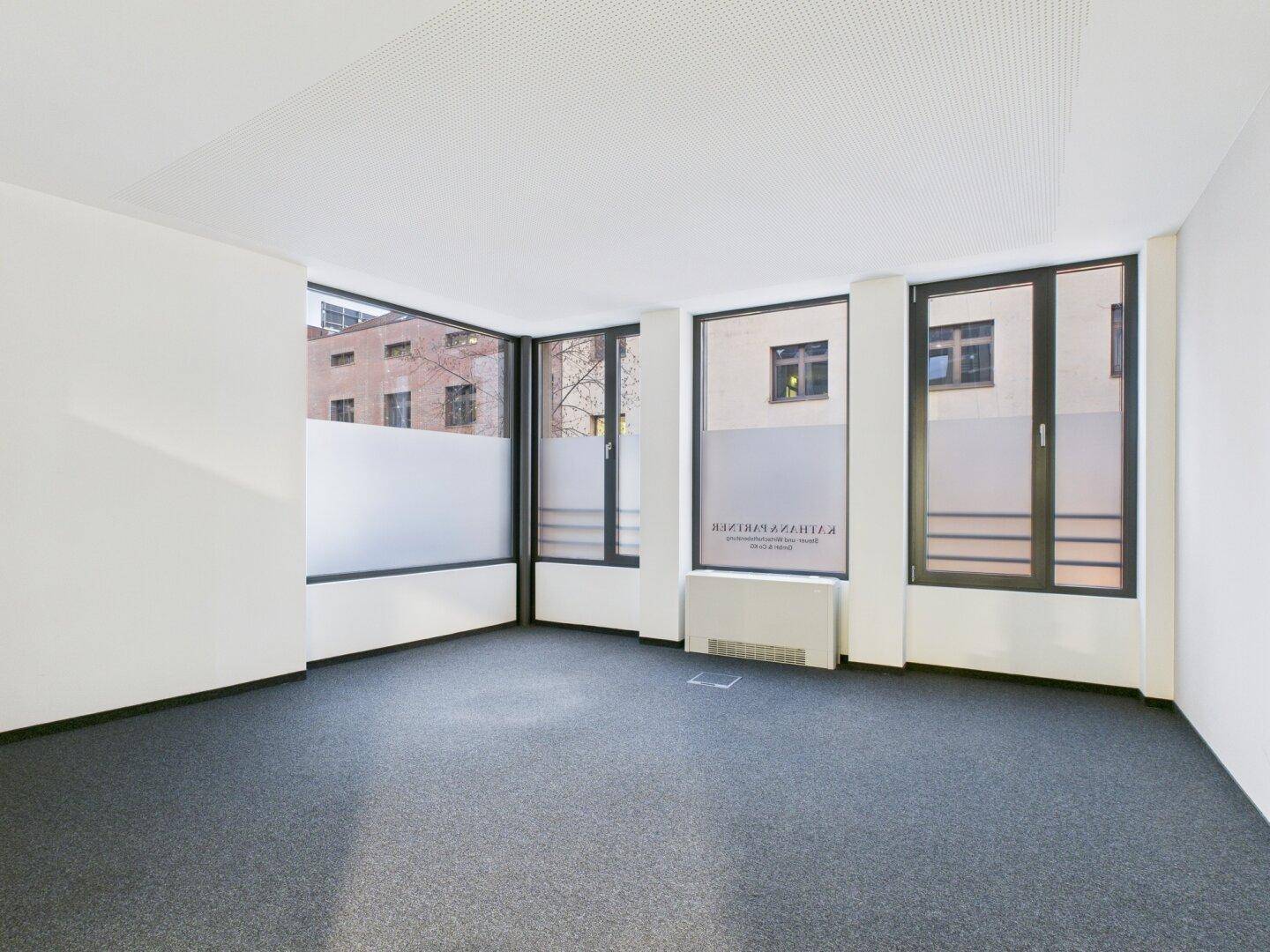Eckbüro mit großen Fenstern, die teilweise mit Milchglasfolie für Privatsphäre versehen sind.