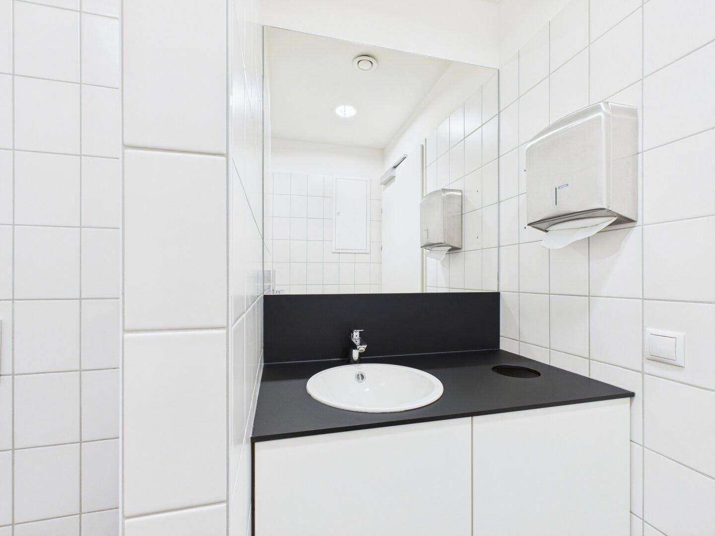 Modernes Badezimmer mit weiß gefliesten Wänden, schwarzer Ablage und ovalem Waschbecken.