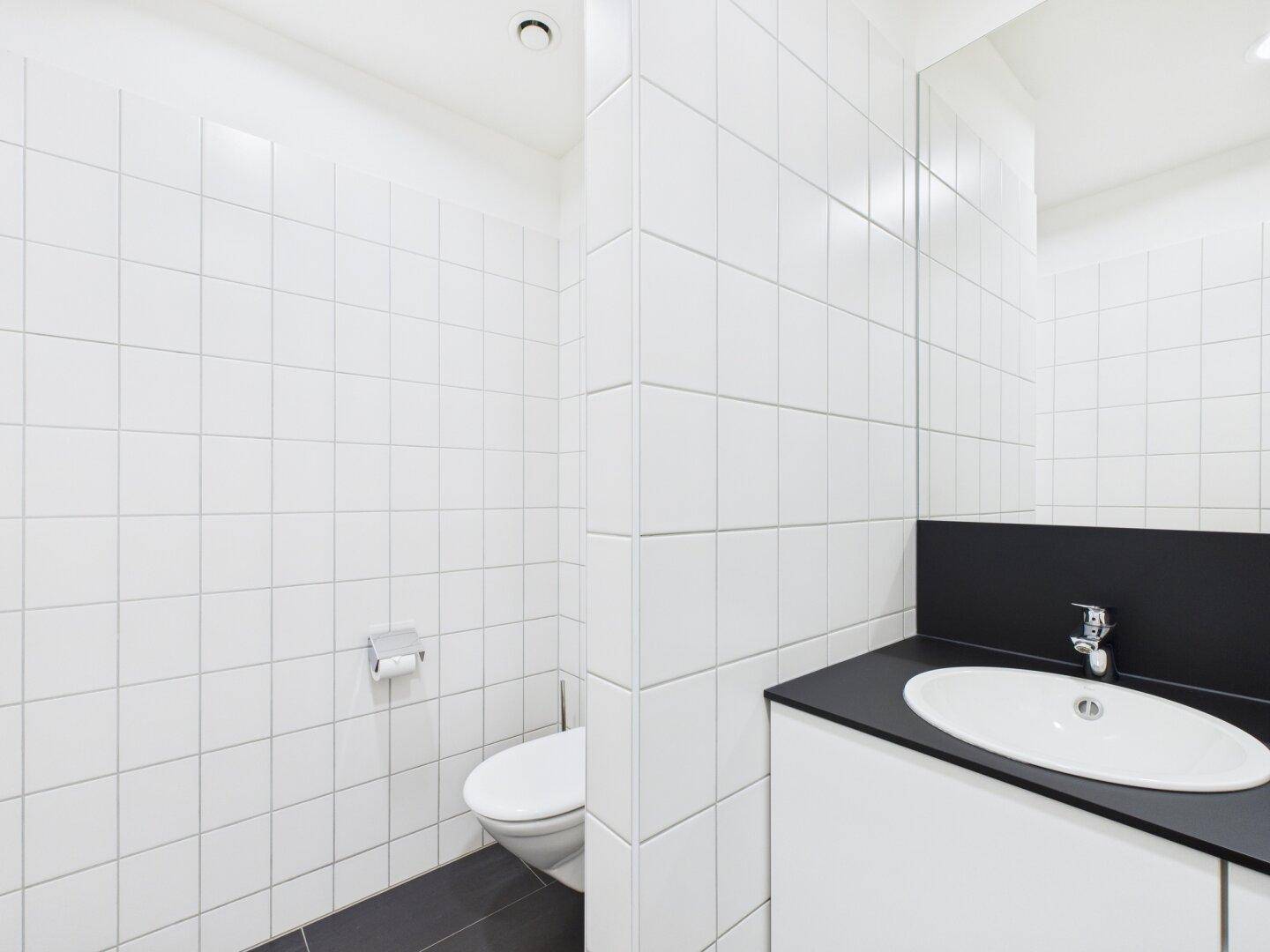 Sauberer Toilettenbereich mit weißen Wandfliesen, dunklem Boden und modernem WC.