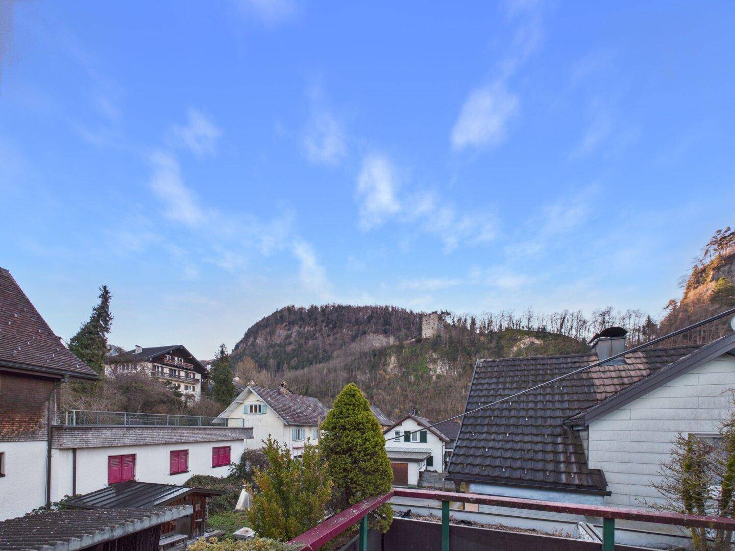 Panoramablick auf eine bergige Landschaft mit Häusern und einem blauen Himmel.