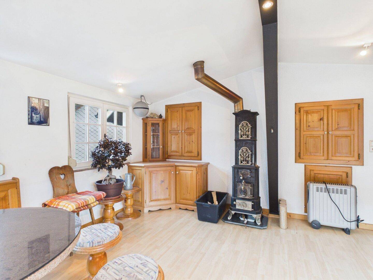 Heller Wohnraum mit Holzboden, freistehendem Ofen und traditionellen Holzmöbeln.