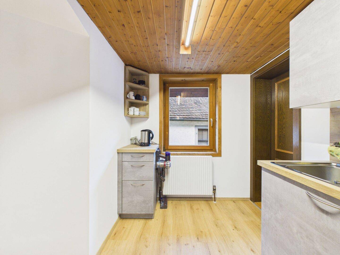 Heller Küchenbereich mit Holzdecke, Fenster und Heizkörper unter der Dachschräge.
