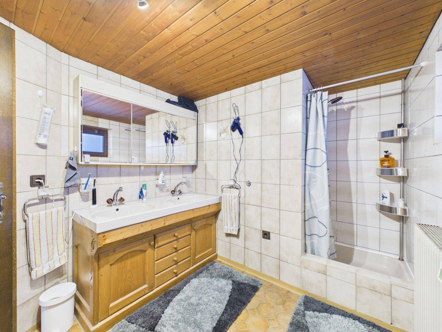 Badezimmer mit Doppelwaschbecken, Badewanne mit Duschvorhang und Holzdecke.