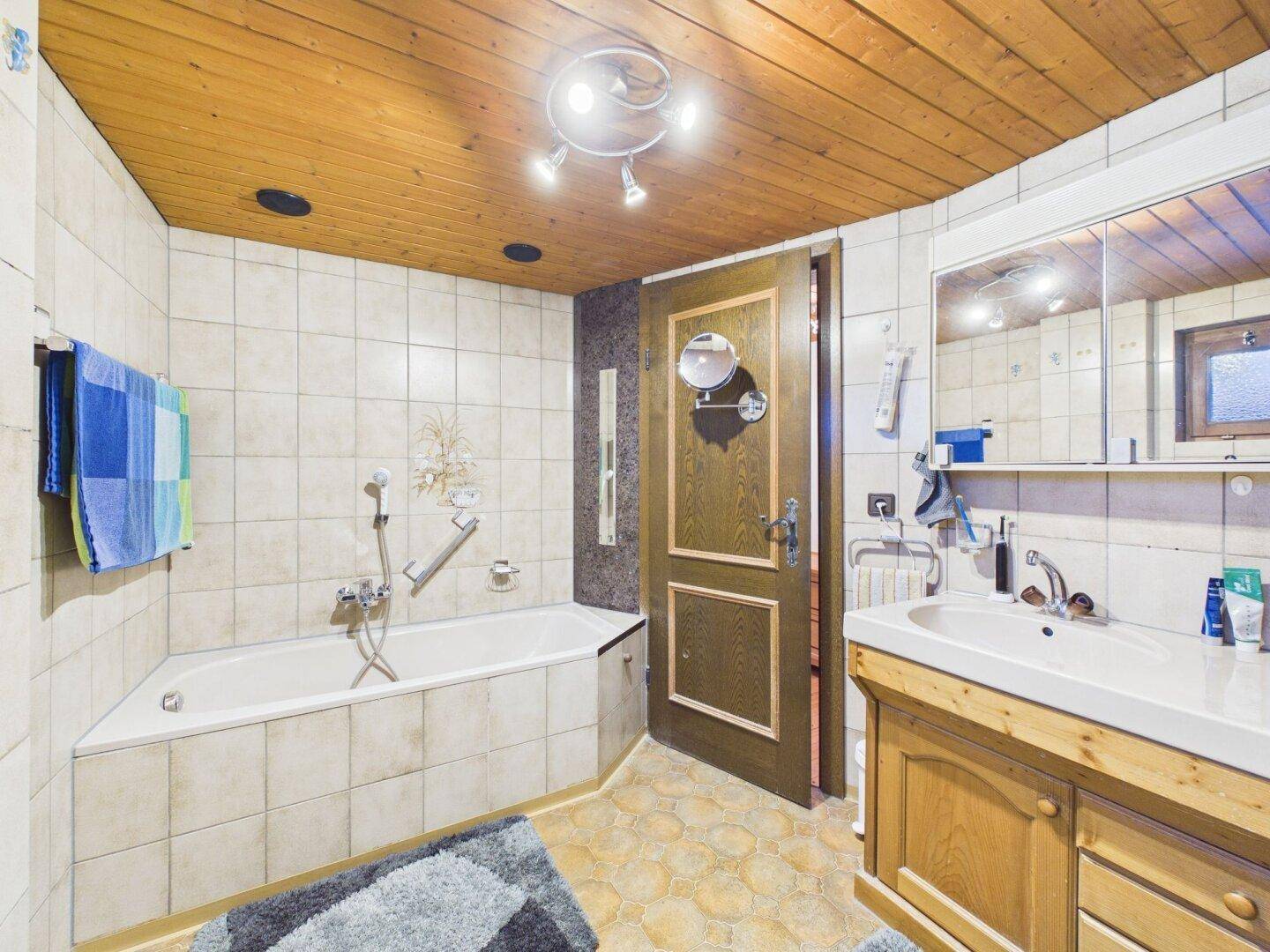 Badezimmer mit Eckbadewanne, Doppelwaschbecken und Holzdecke.