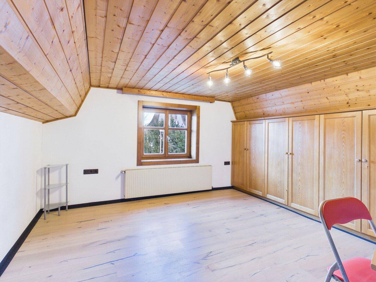 Schlafzimmer mit Dachschräge, Holzdecke, Einbauschränken und Fenster.