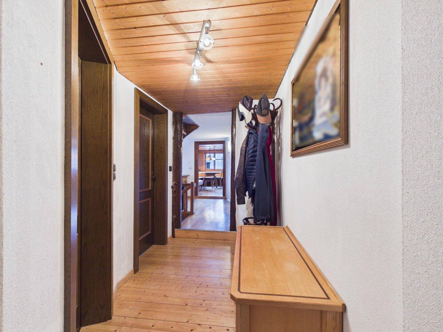 Langer Flur mit Holzfußboden, Garderobe und Blick in den Wohnbereich.