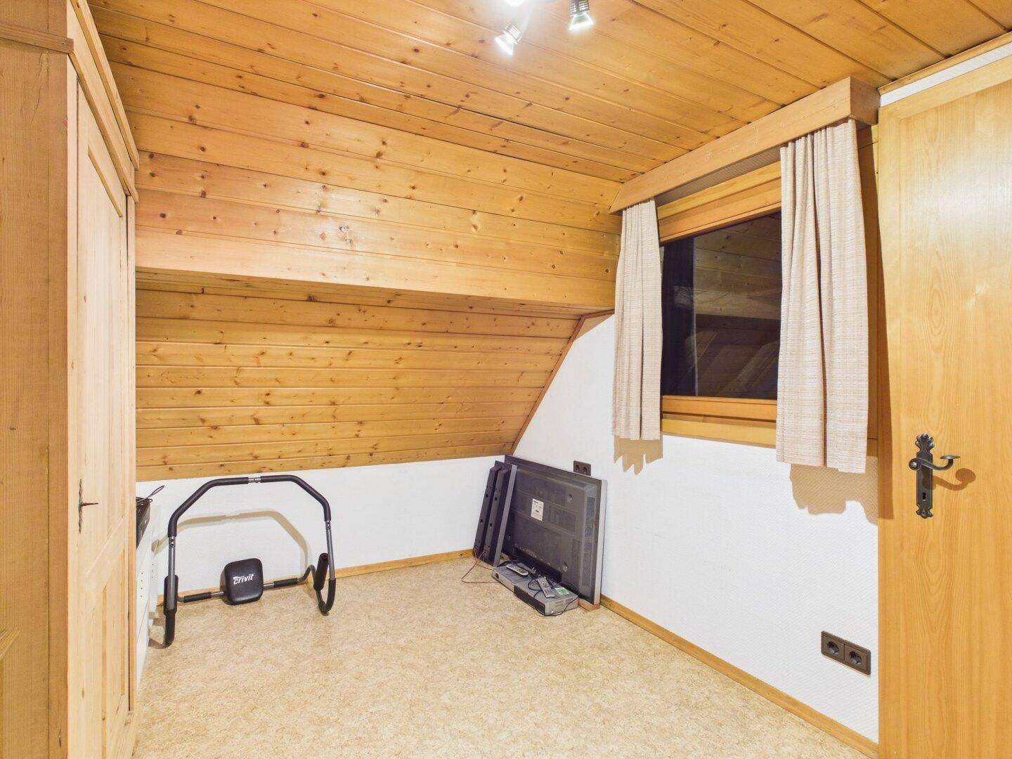 Kleines Schlafzimmer mit Dachschräge, Holzdecke und Fenster.