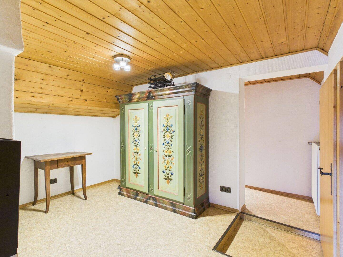 Schlafzimmer mit Dachschräge, Holzdecke und einem traditionellen bemalten Kleiderschrank.