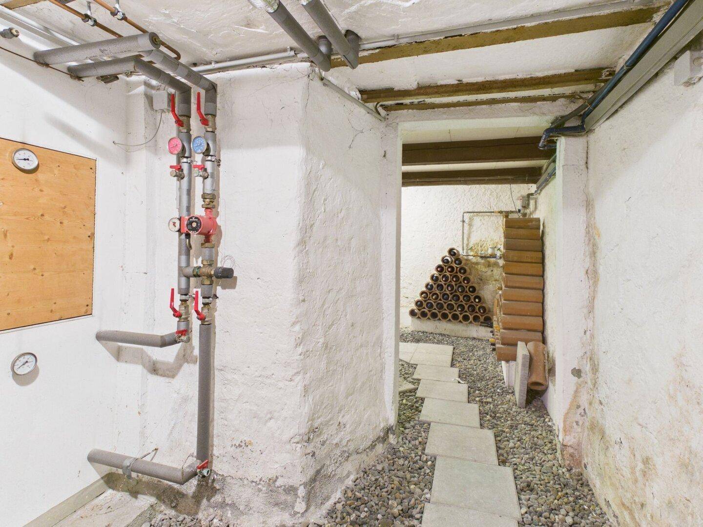 Kellerraum mit Heizungsinstallationen und angrenzendem Bereich zur Weinlagerung.