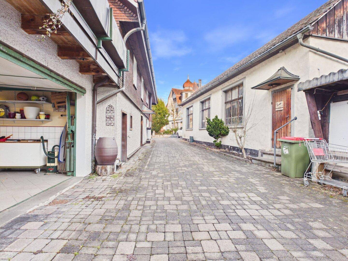 Gepflasterte Zufahrt zwischen zwei Gebäuden mit Zugang zu einer offenen Garage.