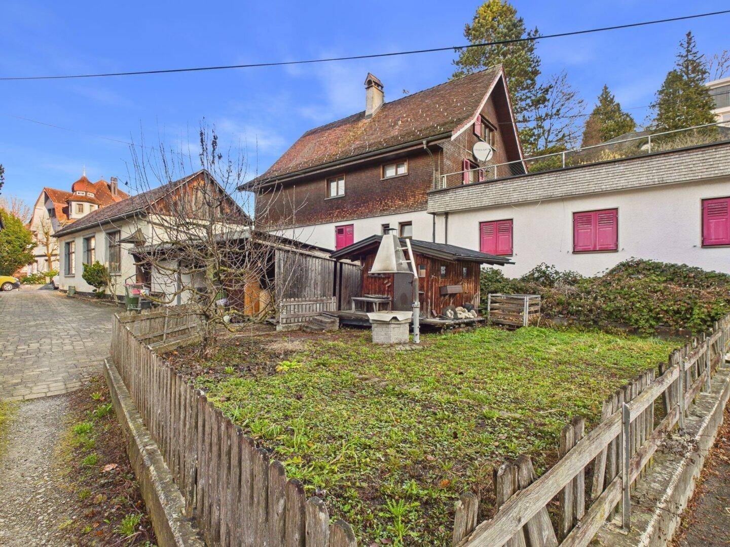 Gartenbereich mit Holzzaun, kleinem Schuppen und Blick auf die umliegenden Gebäude.