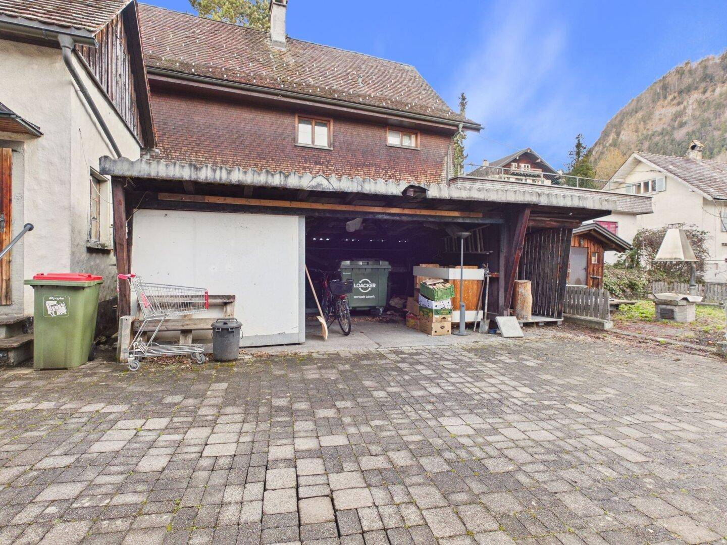 Offene Garage mit gepflastertem Vorplatz und Blick auf die umliegende Berglandschaft.
