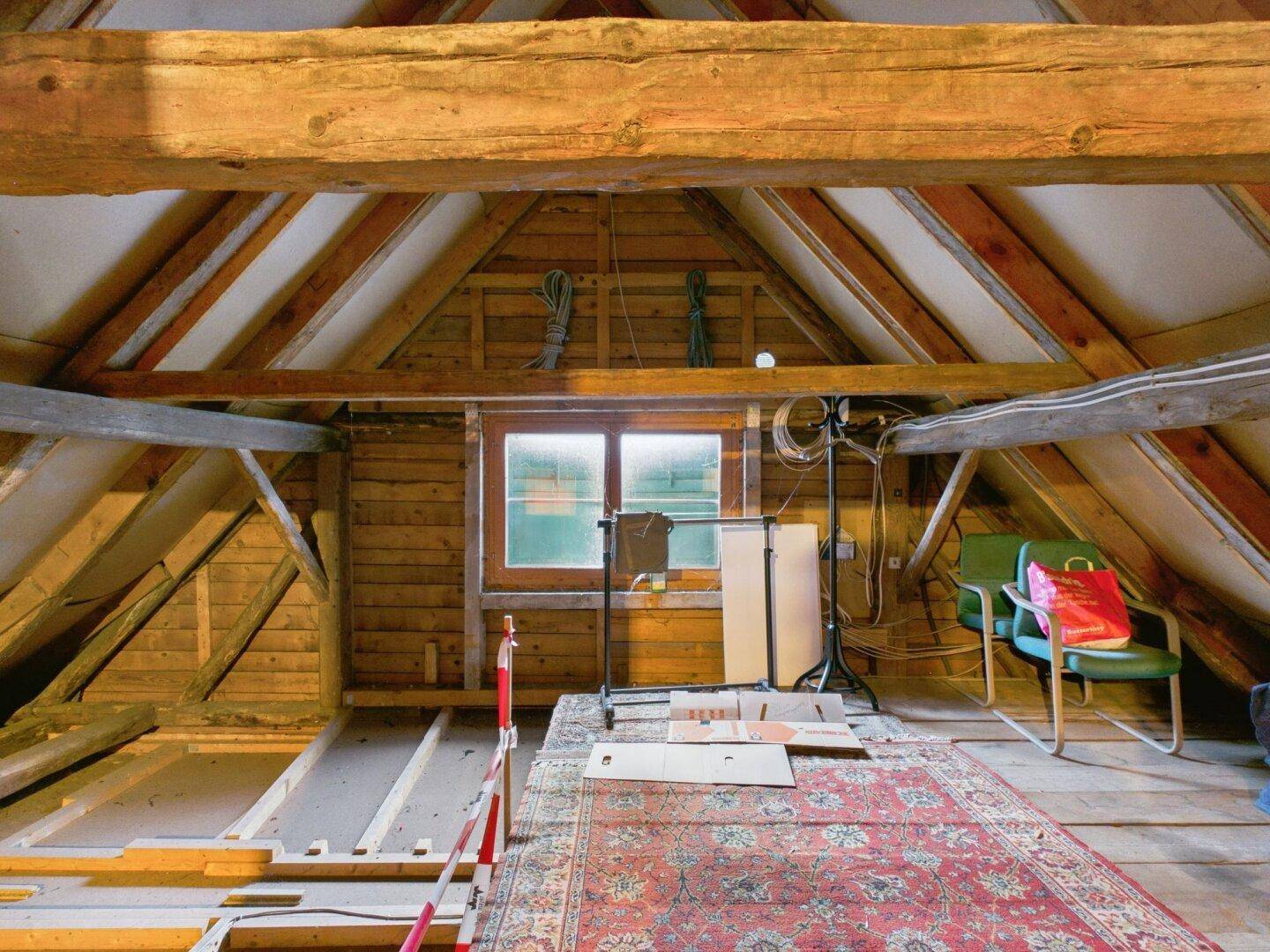 Dachboden mit sichtbaren Holzbalken, Holzverkleidung und natürlichem Lichteinfall durch das Fenster.