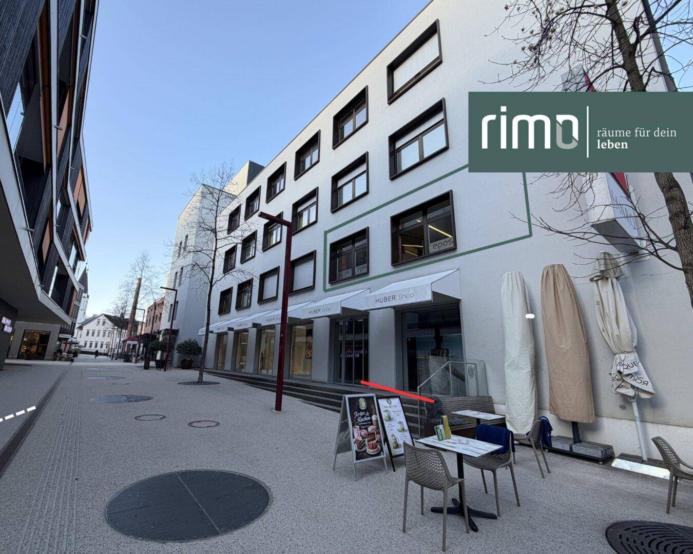 Außenansicht eines Geschäftsgebäudes an einer belebten Straße mit Außengastronomie.