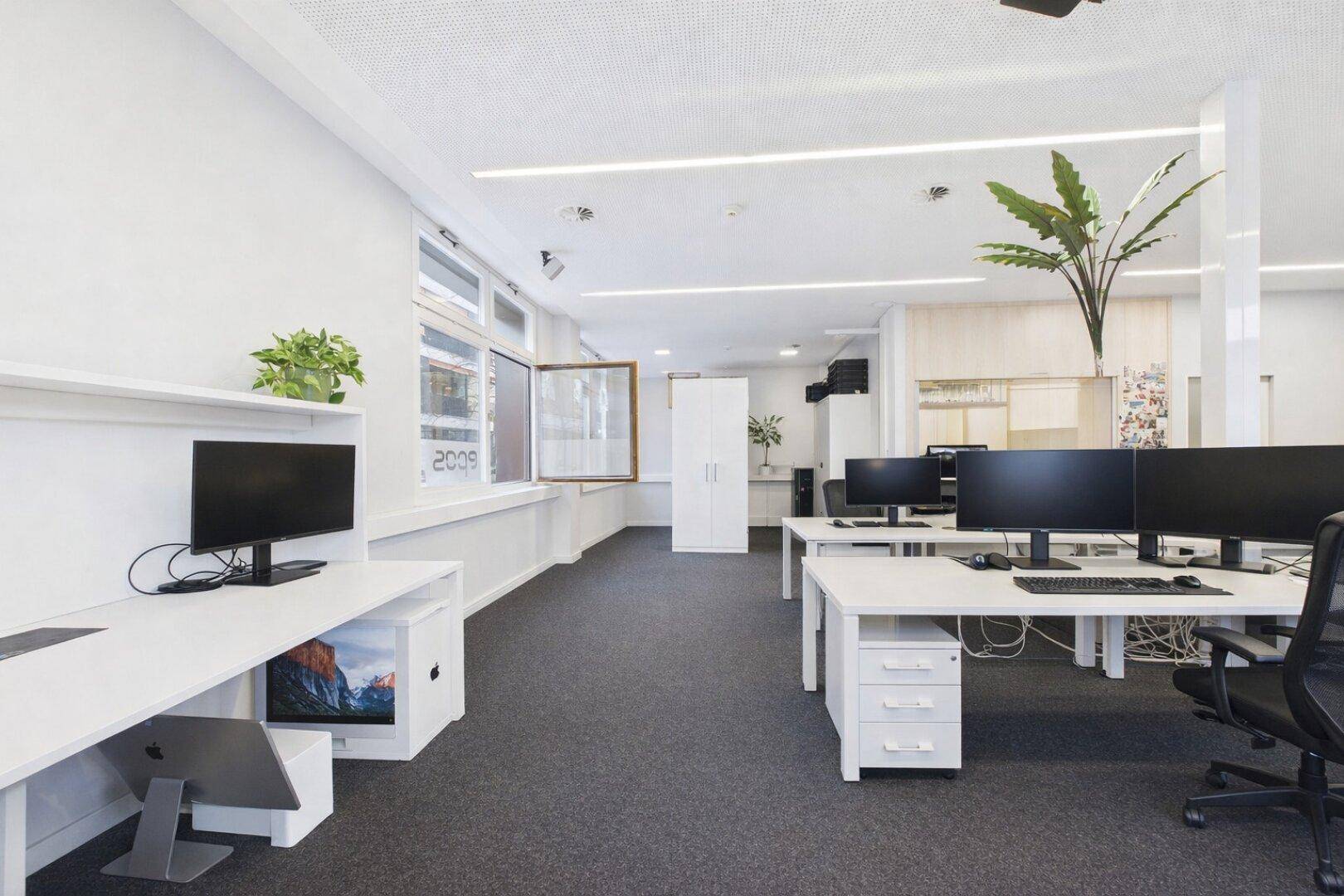 Modernes Büro mit Arbeitsplätzen, Computermonitoren und einem geöffneten Fenster für frische Luft.