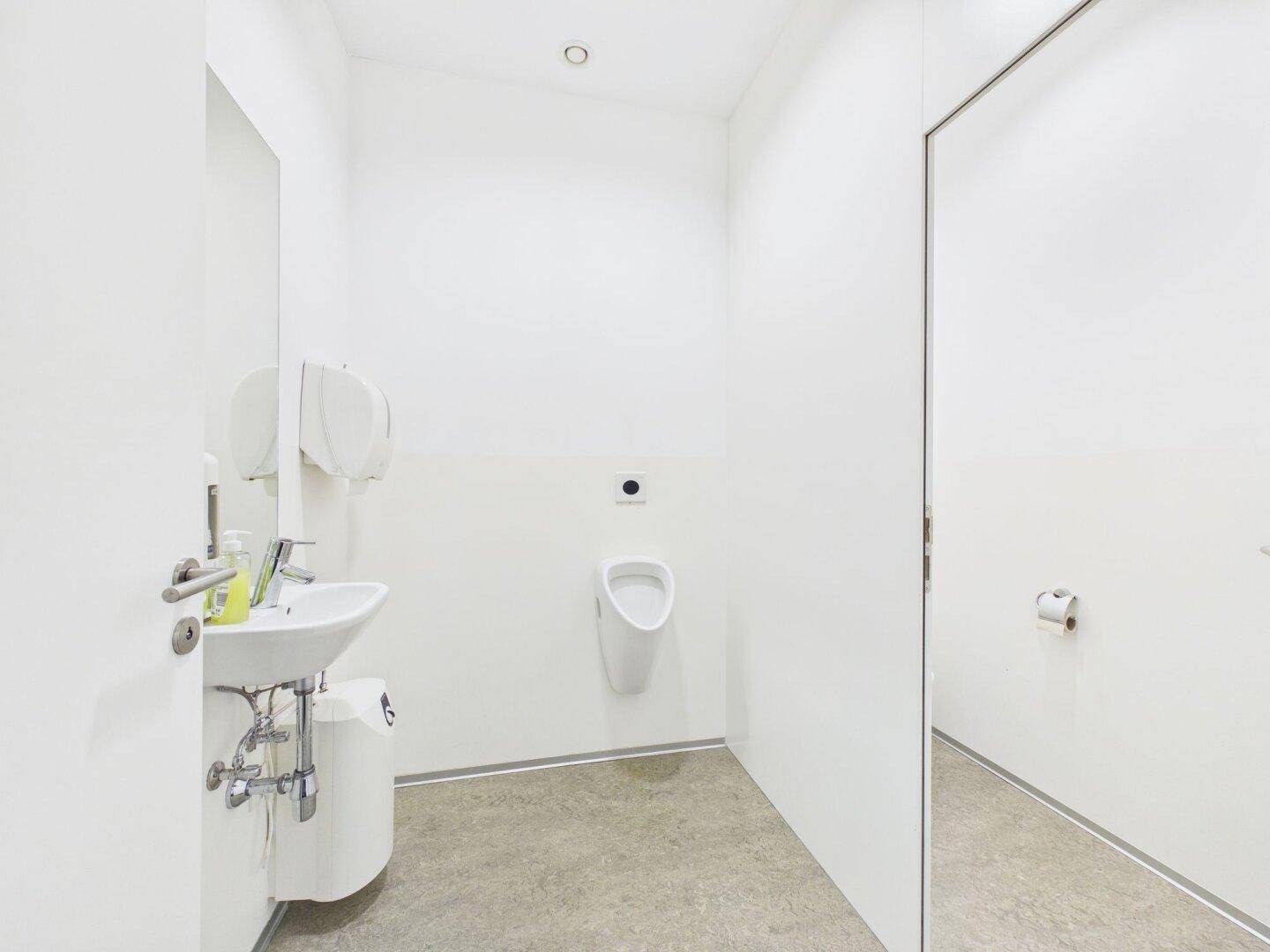 Saubere Herrentoilette mit Urinal, Waschbecken und weiß gefliesten Wänden.