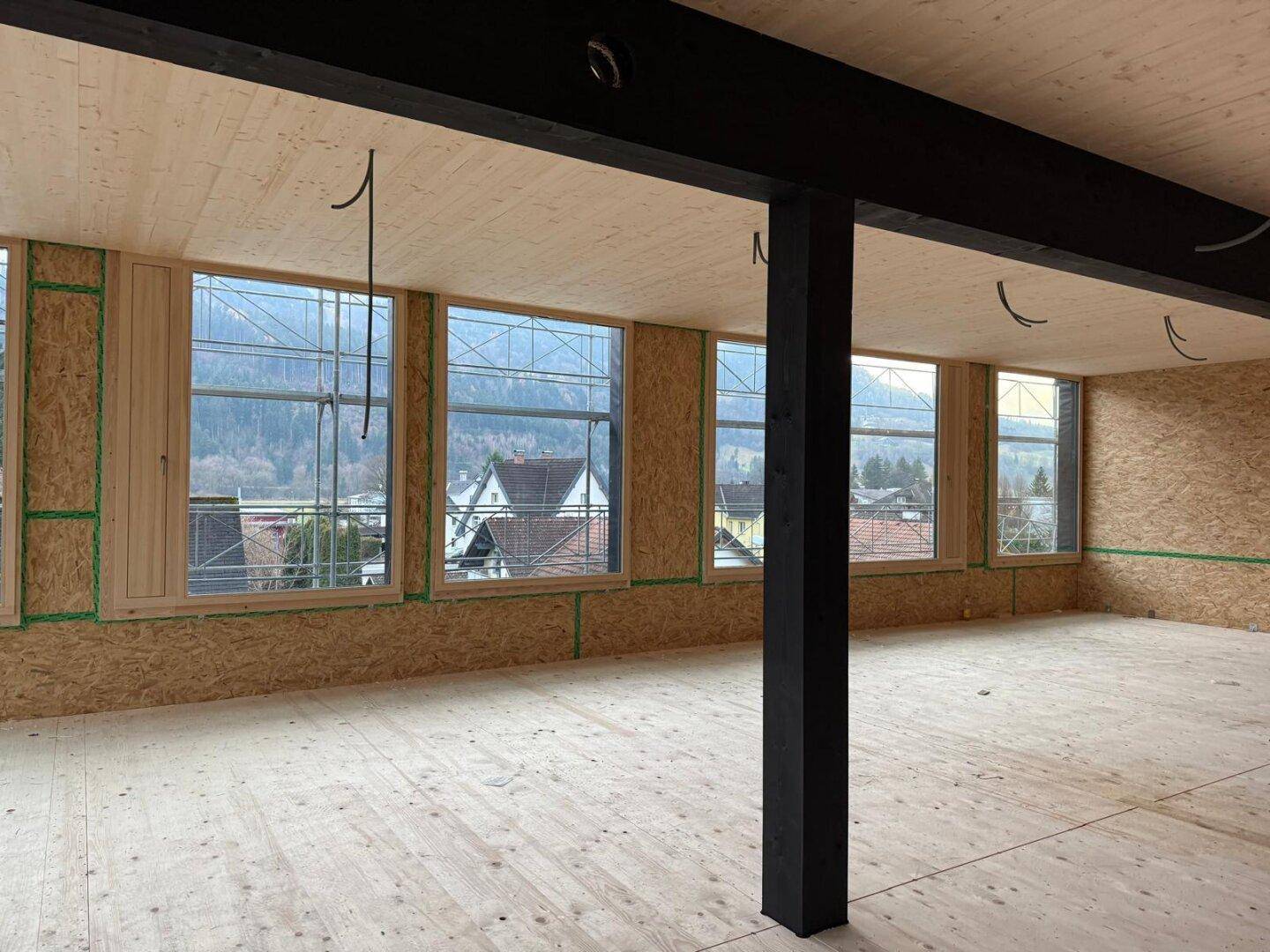 Unfertiger Büroraum mit Holzwänden, großen Fenstern und Blick auf die umliegende Berglandschaft.
