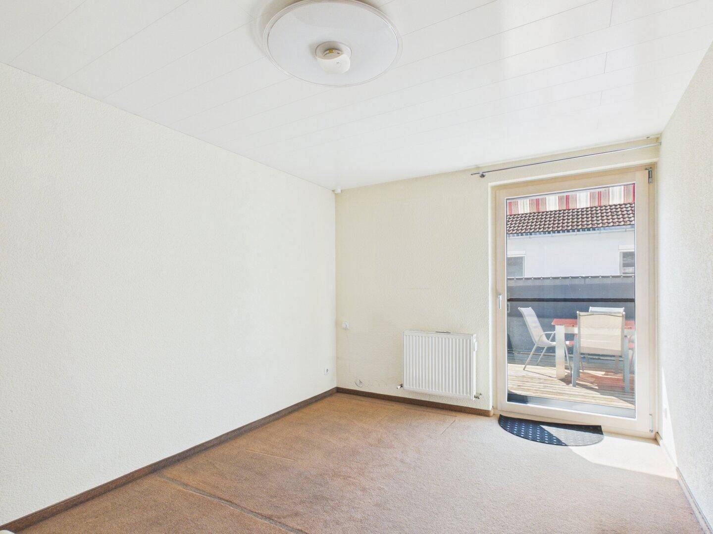 Helles Zimmer mit Teppichboden und direktem Zugang zum Balkon.