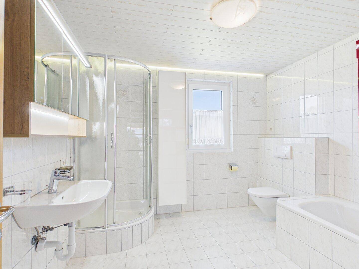 Helles Badezimmer mit Dusche, Badewanne, WC und Fenster.