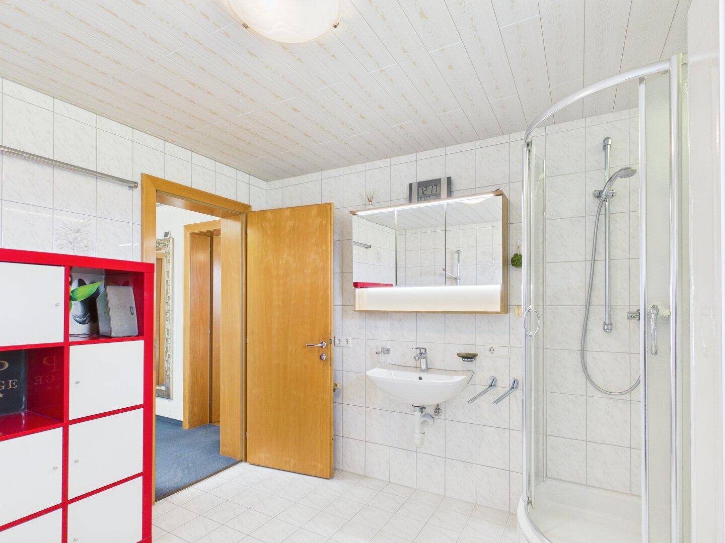 Badezimmer mit Dusche, Waschbecken, Spiegelschrank und Zugang zum Flur.
