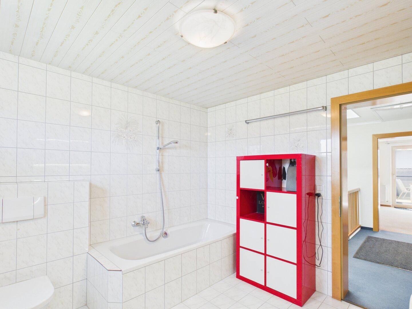 Badezimmer mit Badewanne, Dusche und rotem Regal.
