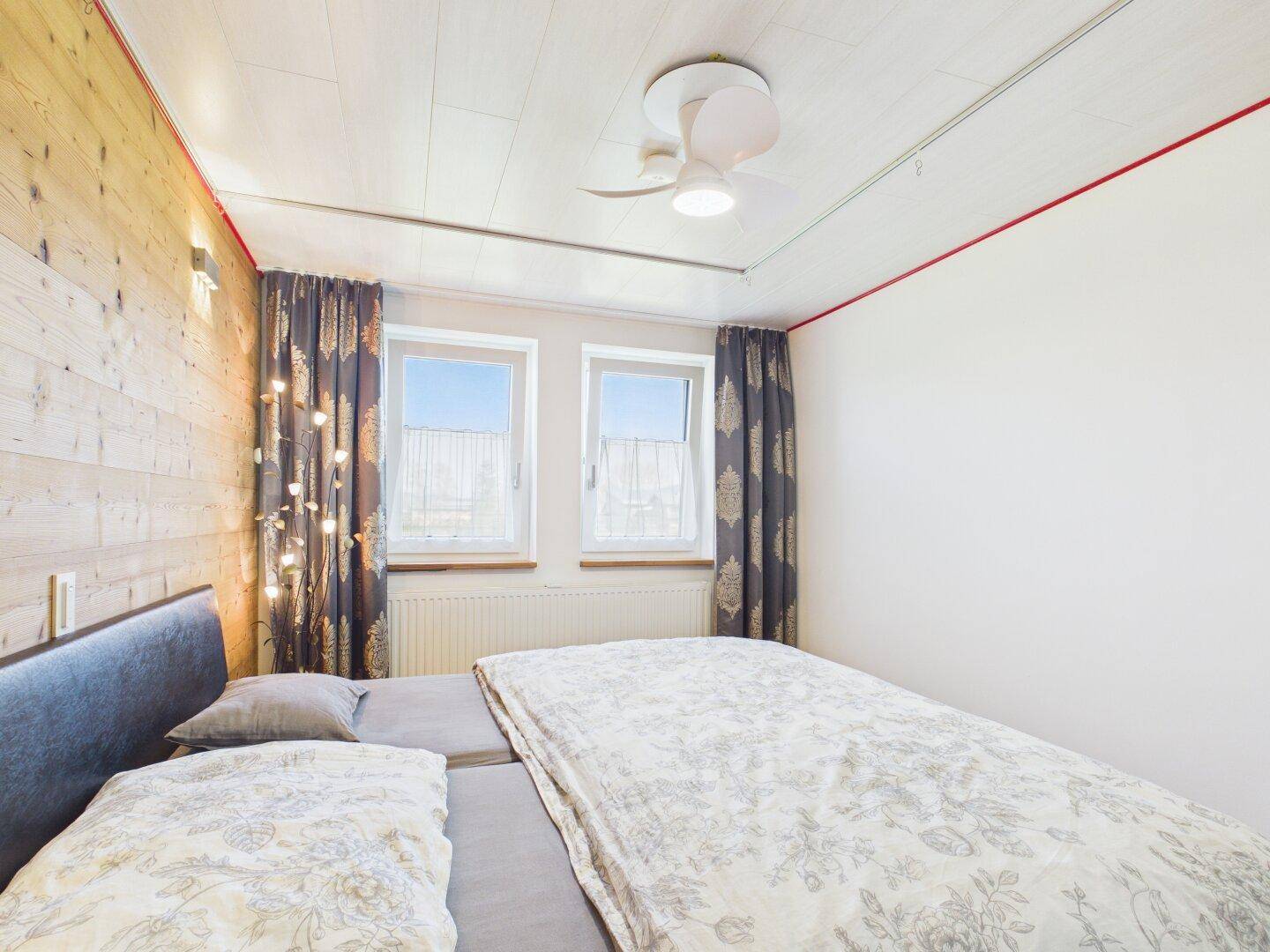 Gemütliches Schlafzimmer mit Holzwand, Doppelbett und Fenster.