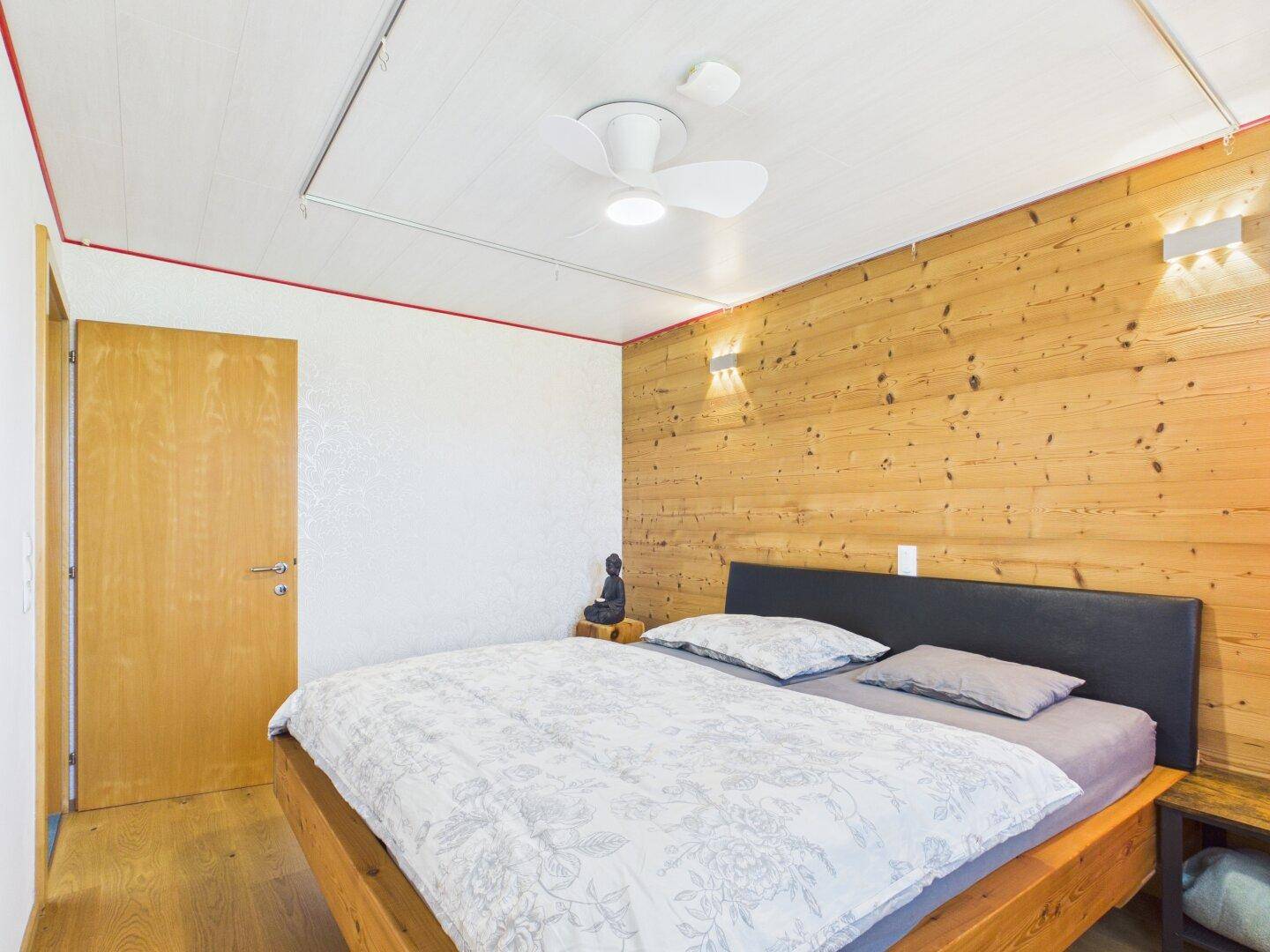 Schlafzimmer mit Holzwand, Doppelbett und Zugang zum Flur.