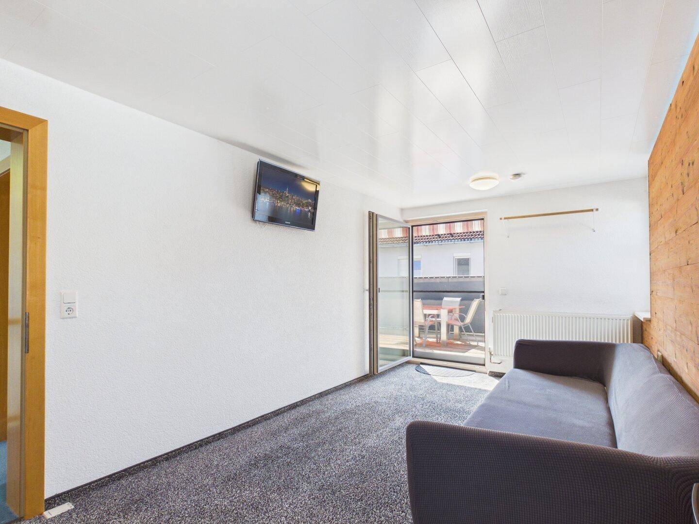 Schlafzimmer mit Teppichboden, Sofa und Zugang zu einem Balkon.