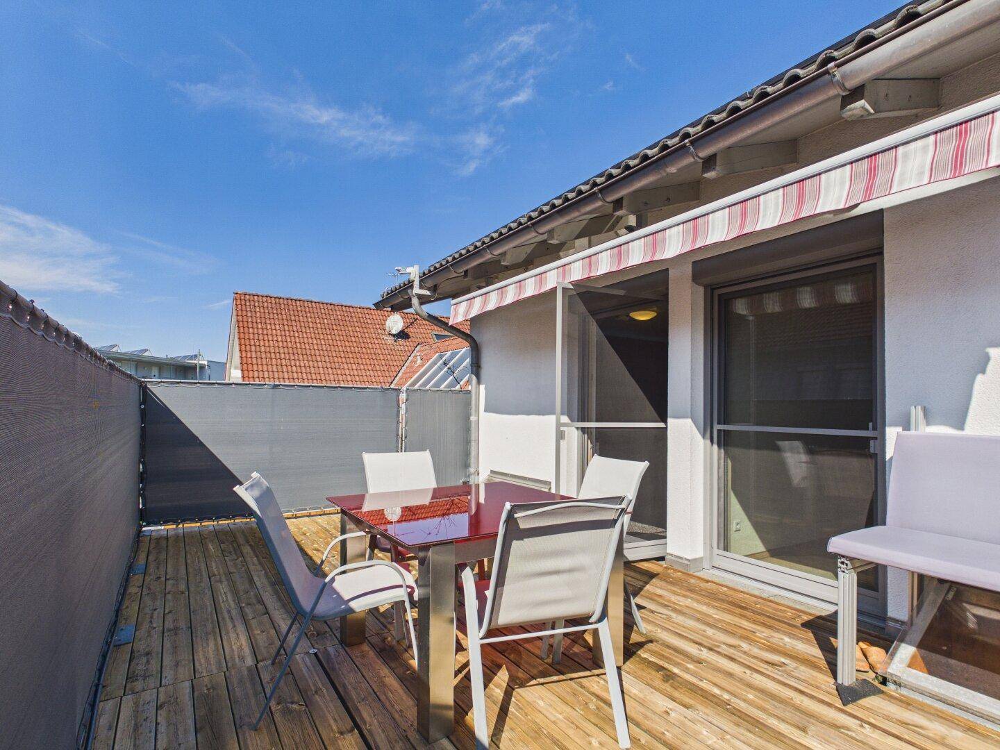 Sonniger Balkon mit Holzboden, Markise und Gartenmöbeln.