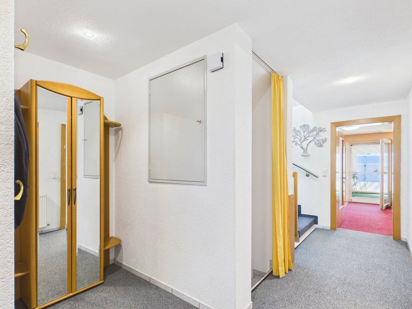 Heller Flur mit Garderobe, Spiegel und Zugang zu weiteren Räumen und Treppe.