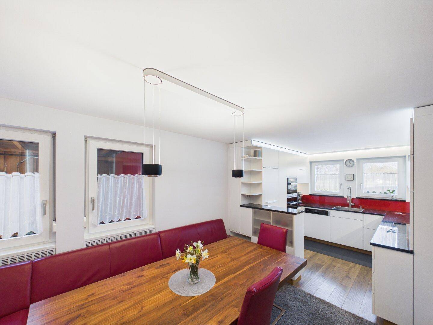 Offener Wohn- und Essbereich mit Holztisch, roter Sitzbank und Blick in die moderne Küche.