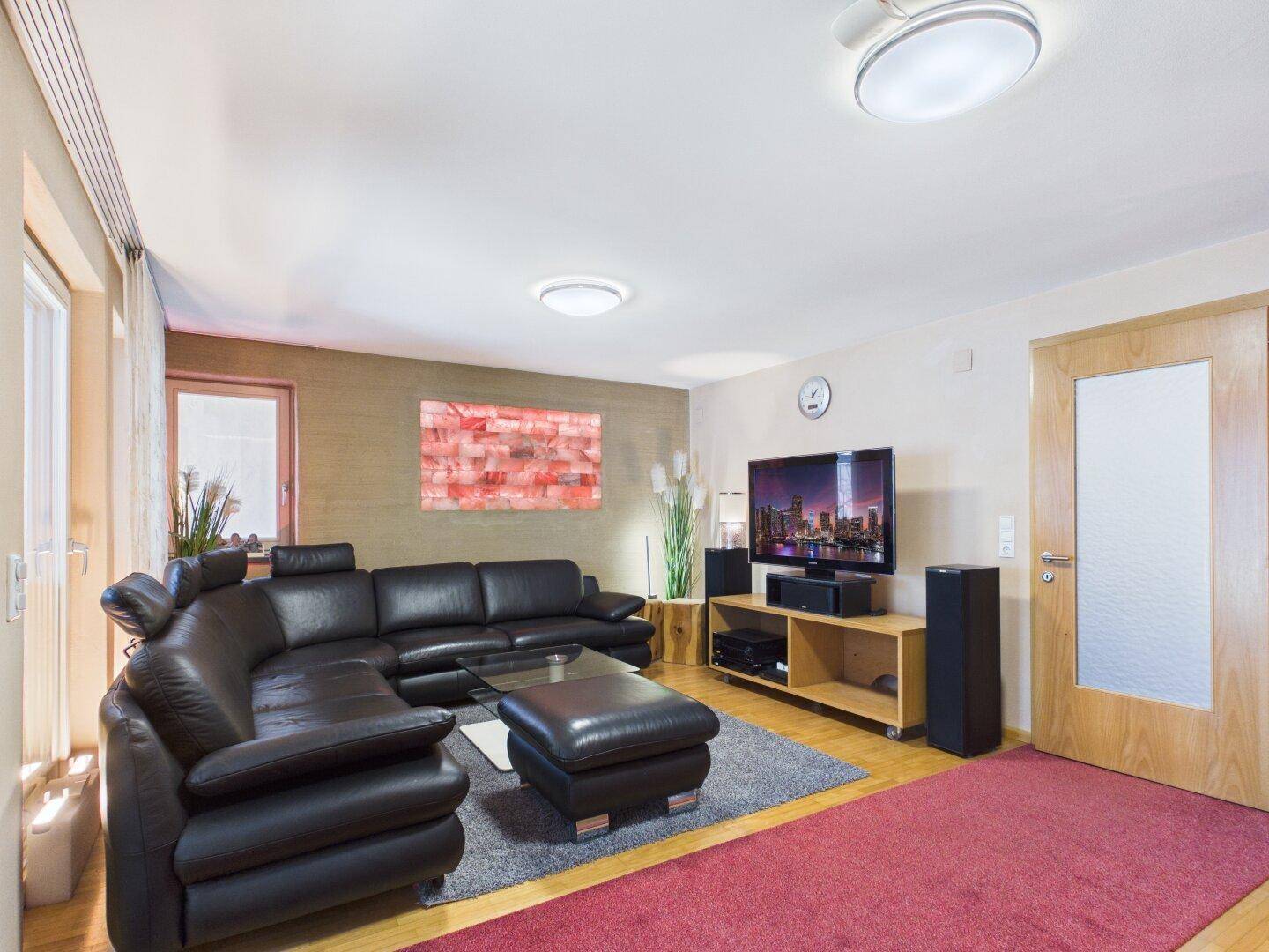Geräumiges Wohnzimmer mit schwarzem Ledersofa, Teppich und TV-Möbeln.