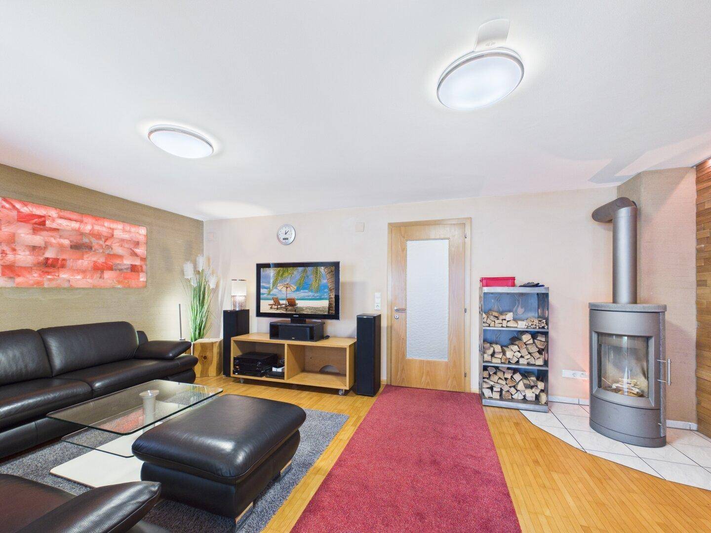 Gemütliches Wohnzimmer mit Kaminofen, Holzboden und schwarzem Ledersofa.