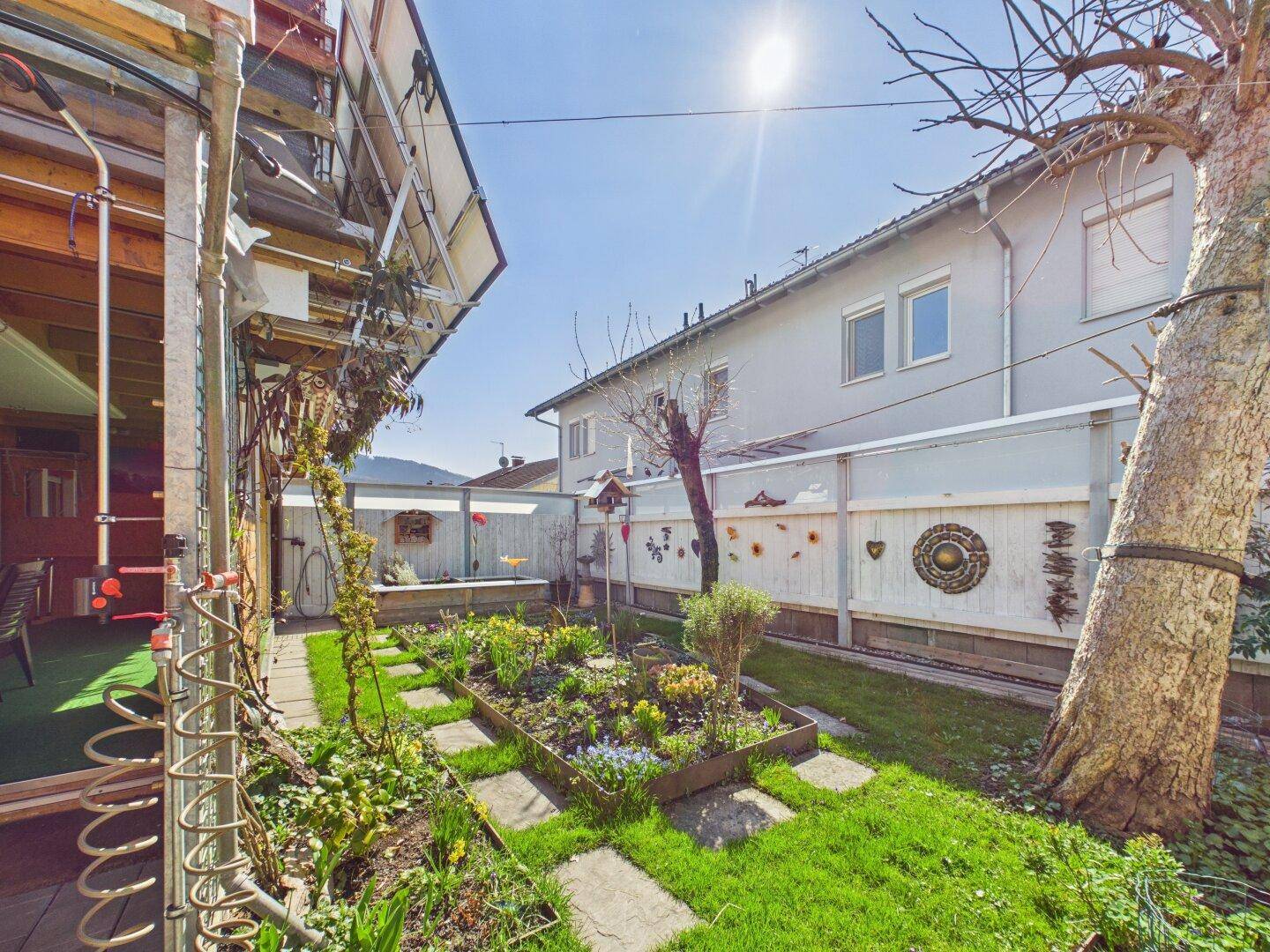 Sonniger Garten mit Rasen, Blumenbeeten und Blick auf die Nachbarhäuser.