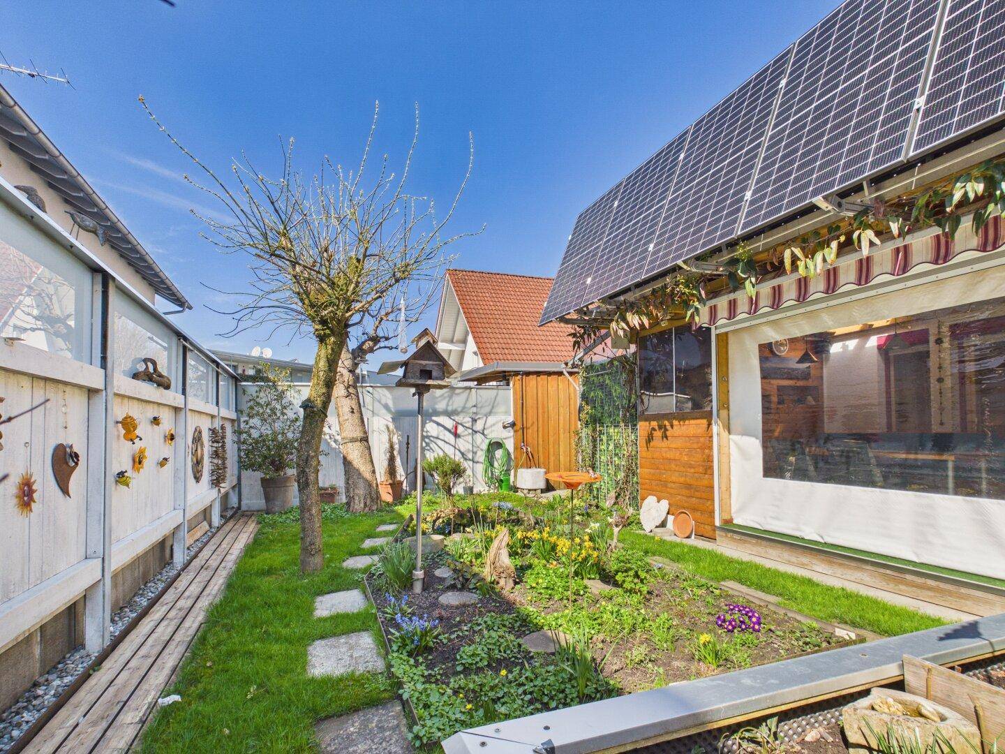 Gepflegter Garten mit Hochbeeten, Rasenfläche und Solaranlage auf dem Dach.