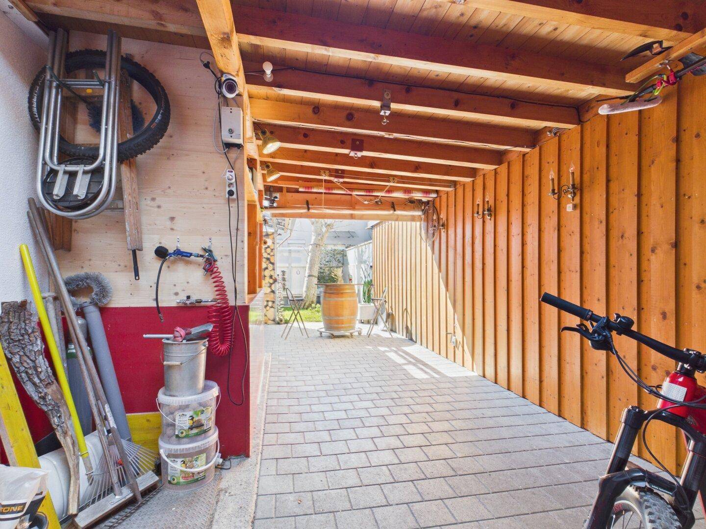 Überdachter Außenbereich mit Holzwänden, Pflastersteinen und Abstellmöglichkeiten.