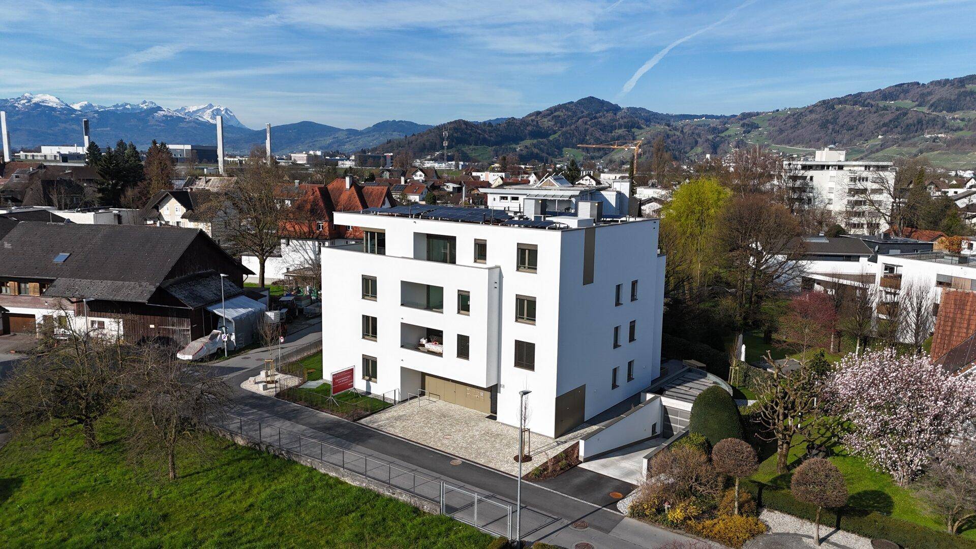 Modernes Wohnhaus mit weißer Fassade, Solaranlage und Blick auf die schneebedeckten Berge im Hintergrund.