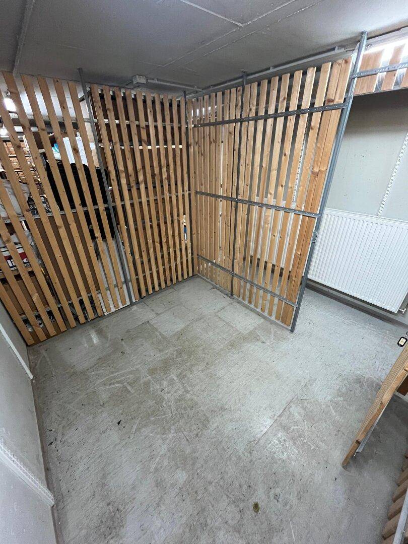 Geräumiges Kellerabteil mit Betonboden und Holzabtrennungen, inklusive Heizkörper an der Wand für Temperierung.