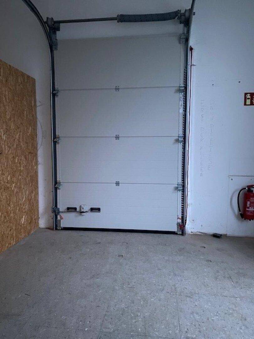 Innenansicht einer Garage oder Lagerhalle mit einem großen weißen Rolltor und Betonboden.