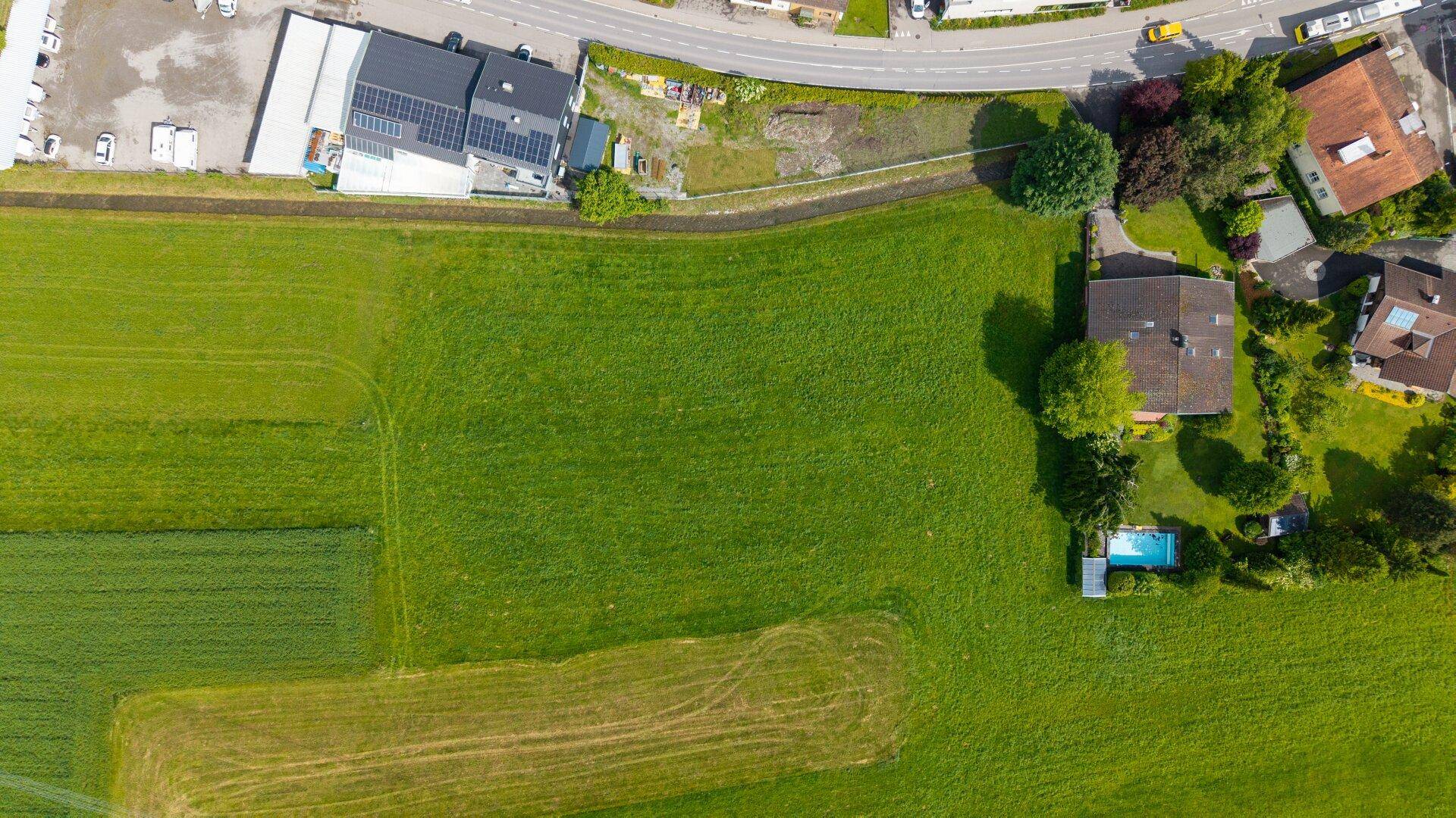 Luftaufnahme von weitläufigen Feldern und einer Wohnsiedlung mit angrenzender Straße.