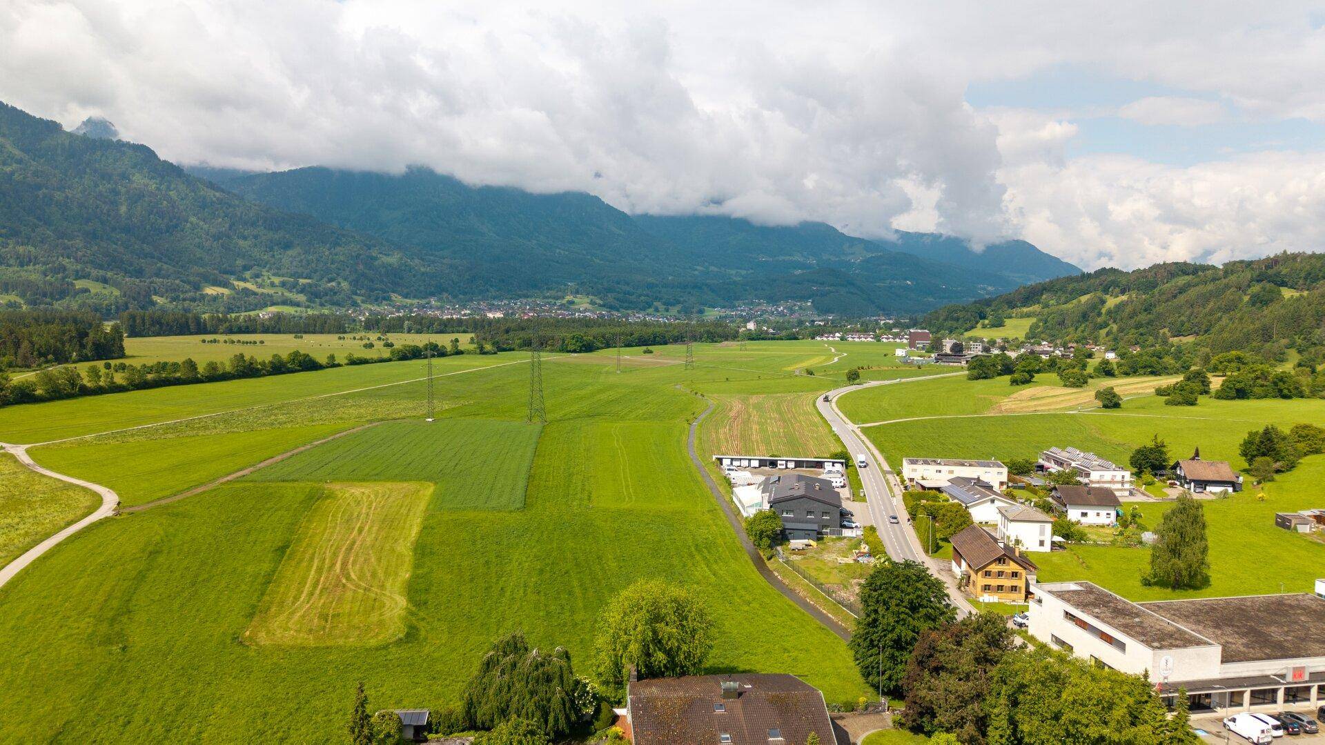Luftaufnahme eines Tals mit landwirtschaftlichen Flächen, Wohngebieten und einer Straße.