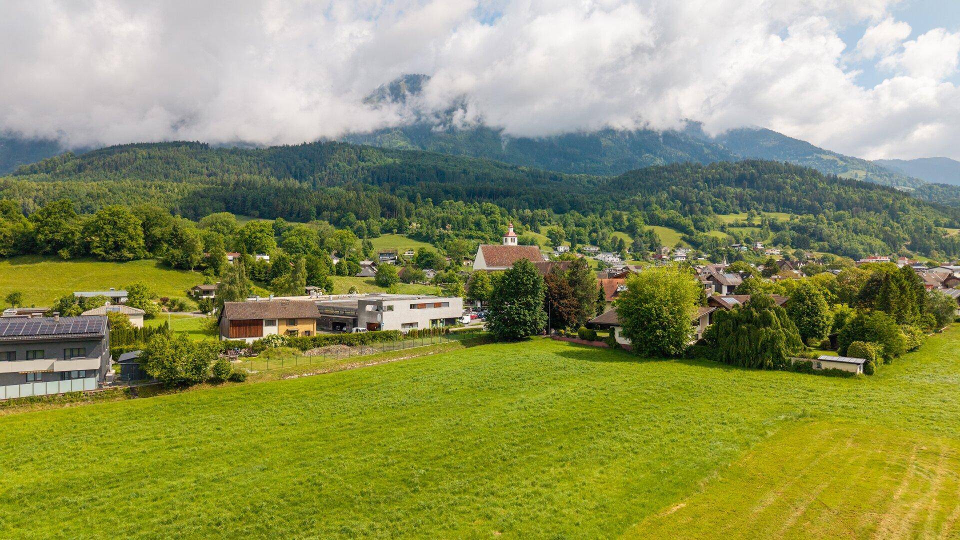 Weitläufiger Blick auf ein charmantes Dorf mit Kirche, eingebettet in grüne Natur und Berge.
