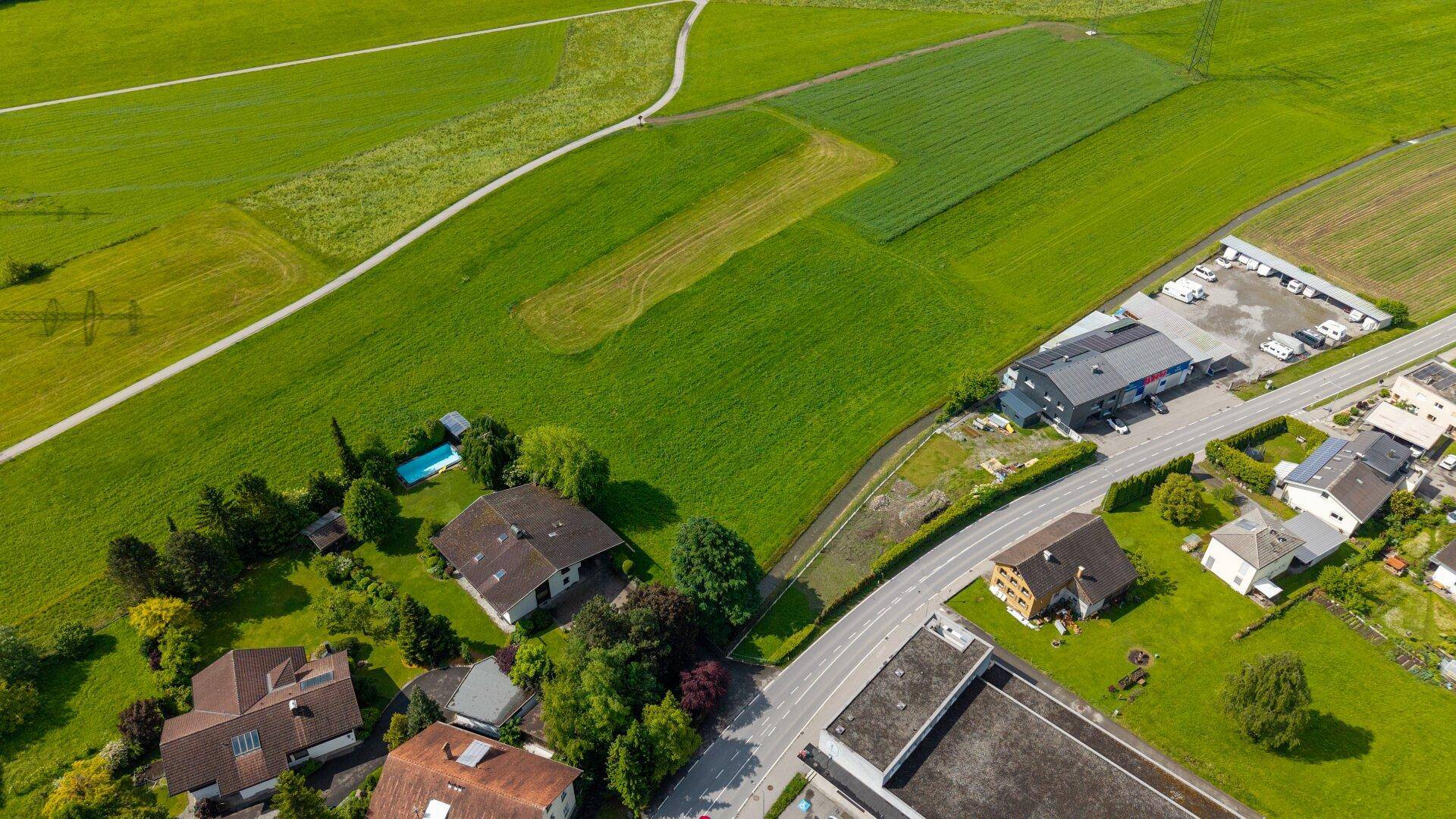 Luftaufnahme von grünen Feldern, einer Straße und angrenzenden Wohnhäusern.