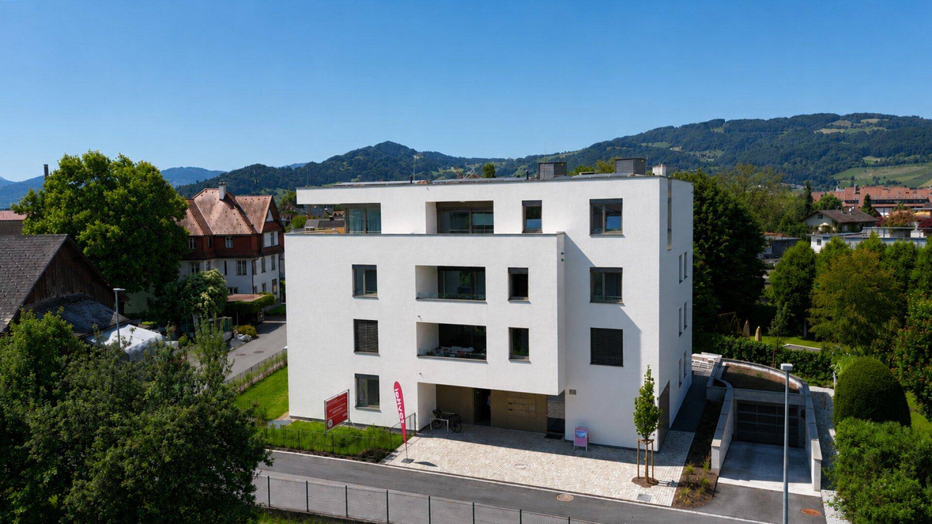 Moderne Wohnanlage mit weißer Fassade und Bergblick in grüner Umgebung.