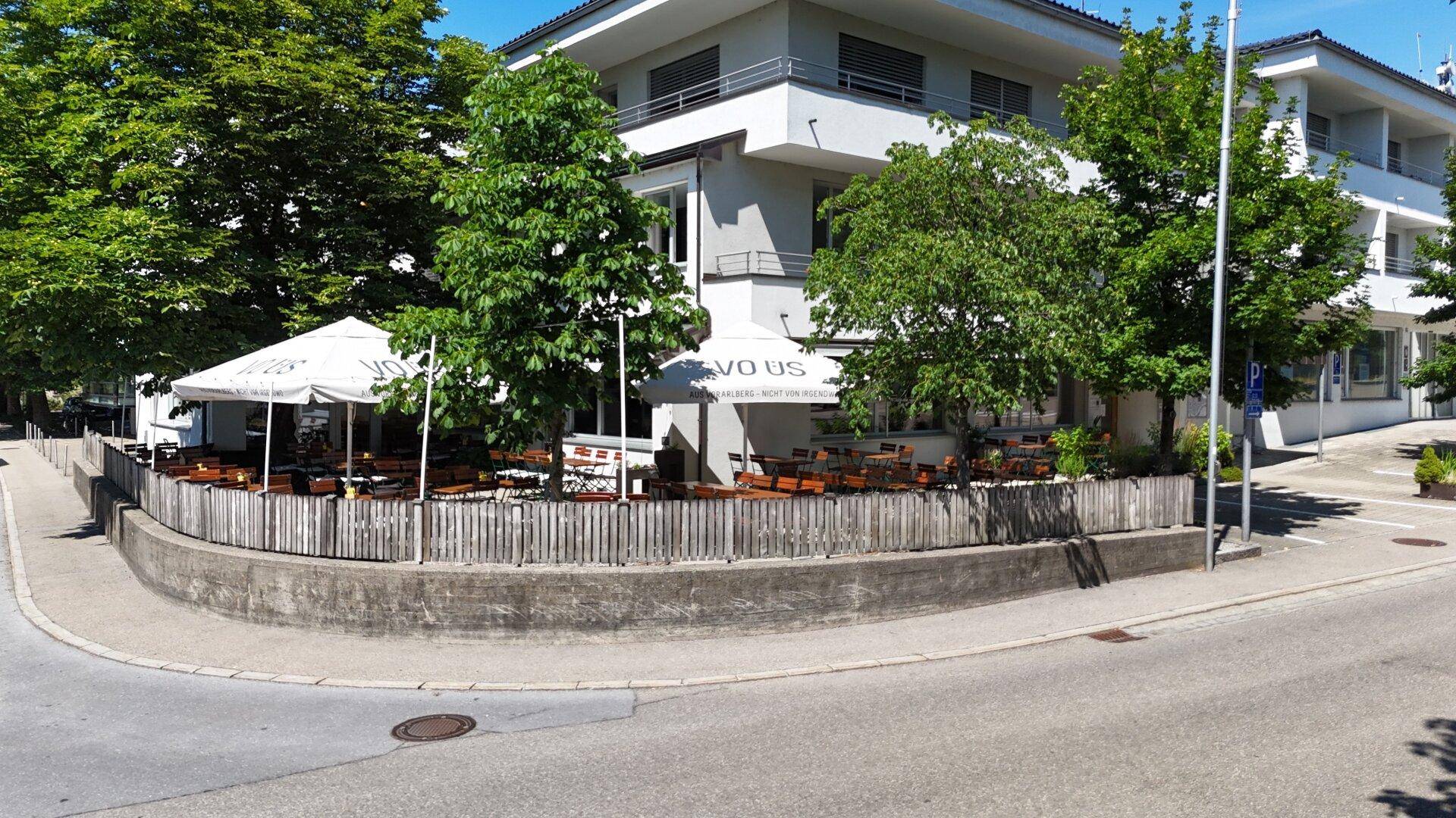 Eine weitläufige Außenterrasse eines Restaurants mit vielen Tischen, Stühlen und Sonnenschirmen, umgeben von Bäumen.