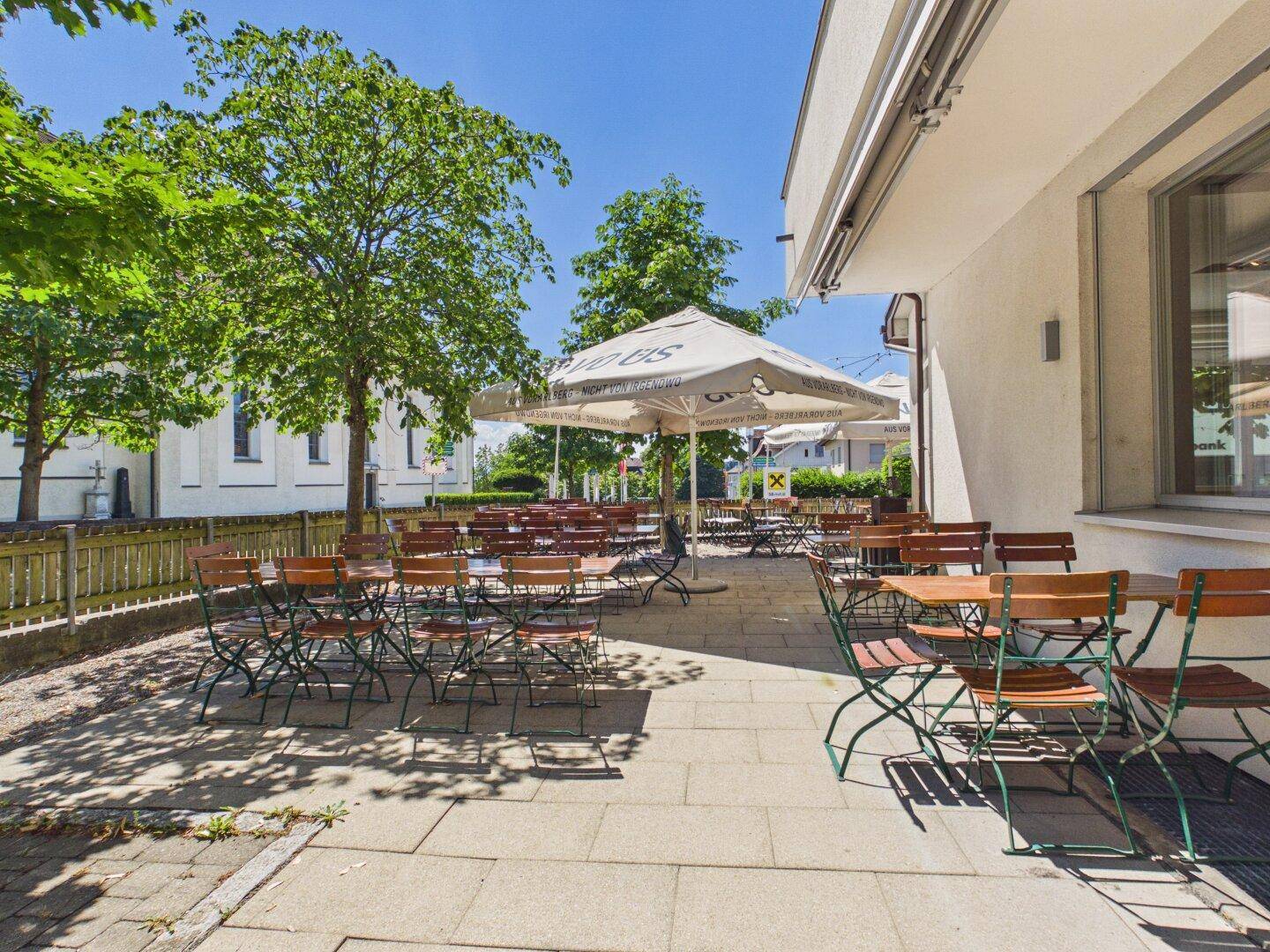 Eine geräumige, gepflasterte Restaurantterrasse mit zahlreichen Tischen und Stühlen, direkt am Gebäude gelegen.