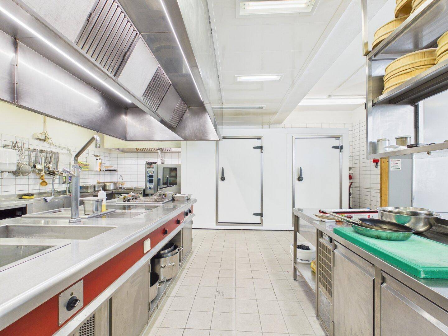 Professionelle Großküche mit Edelstahloberflächen, großen Dunstabzugshauben und industriellen Kühlräumen.